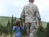 A man in military uniform is walking away from the camera holding the hand of a young child.