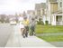 A man in uniform and a woman in a dress walking down the sidewalk with their two children riding bikes ahead of them. | North Haven Communities at Fort Wainwright