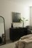 Elegant bedroom interior with a sleek black dresser, modern artwork, and vibrant green plant.