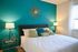 Elegant bedroom with vibrant teal accent wall, sumptuous bed with plush pillows, and stylish decor; ideal for a serene retreat.
