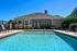 Inviting outdoor pool area with crystal-clear water, lounge chairs, and a charming clubhouse under a bright blue sky.