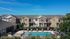 Charming townhouse complex with a sparkling pool and sun loungers, perfect for relaxation under a clear blue sky.