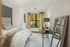 Cozy bedroom with stylish decor, featuring a plush bed, large window with lush views, elegant mirror, and chic lighting.