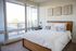 Bright and airy bedroom with a cozy bed, large windows offering a beautiful view, and elegant wall art, perfect for relaxation.