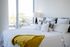 Bright and airy bedroom showcasing a luxurious bed with crisp white linens and vibrant yellow accents, framed by large windows with a stunning view.