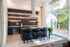 Sleek modern kitchen with an island, large windows, elegant black cabinetry, and open shelving filled with glassware and greenery.