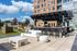 Modern outdoor patio with stylish seating, a sleek bar area under a pergola, and scenic views of a vibrant urban landscape.