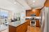 Modern apartment interior with sleek open-plan kitchen featuring stainless steel appliances, a polished granite island, and warm wood cabinetry; inviting living area with stylish decor and expansive city views through large windows.
