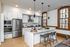 Modern kitchen with sleek white cabinetry, stainless steel appliances, and a stylish island with barstools, complemented by large windows and elegant pendant lighting.