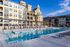 Luxurious apartment complex with historic architecture and a modern outdoor pool under a clear blue sky.
