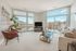 Bright and modern living room with floor-to-ceiling windows offering sweeping city views, plush seating, and chic decor.