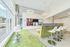 Modern and inviting lounge area with sleek bar stools, a green sofa with high backrests, and a wall-mounted multi-screen display. Large windows offer ample natural light, complemented by stylish circular overhead lighting.