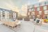 Chic outdoor patio with modern seating overlooking elegant urban apartment complex at sunset.
