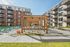 Modern apartment complex with stylish outdoor seating area, featuring sunlit lounge chairs and a sleek pergola, perfect for relaxation and social gatherings.