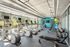 Modern fitness center with large windows, featuring treadmills, elliptical machines, free weights, and a vibrant blue accent wall.