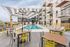 Modern apartment complex with stylish pool area, featuring sun loungers and chic outdoor seating under a striped umbrella.