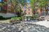 Charming outdoor courtyard featuring lush greenery, barbecue grills, and inviting picnic tables, perfect for relaxing and entertaining.