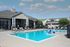 Inviting outdoor pool area with sun loungers, clubhouse, and beautifully manicured surroundings under a bright blue sky.