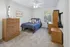 Inviting bedroom featuring a cozy bed with vibrant pillows, a stylish wooden dresser, and a functional desk area under natural light.
