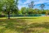 Lush green park view with a tennis court and tall trees under a bright blue sky, offering a serene recreational space.