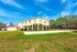 Bright and inviting exterior of a property featuring an elevated structure and a well-maintained sand volleyball court, surrounded by lush greenery under a clear blue sky.