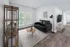 Chic living room with modern black sofa, stylish artwork, sleek floor lamp, and glass double doors opening to a lush view, highlighted by elegant wood flooring.