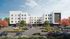 Modern apartment complex with sleek exterior design, surrounded by landscaped greenery and vibrant urban trees, featuring ample parking.