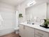 Glendale, AZ, Apartments - Acero at the Stadium - Bathroom with White Quartz Counter Sink, Off-White Cabinetry, a Large Mirror, and a Shower with a Tub and White Shower Curtain.