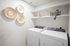 Three-Bedroom Apartments in West Phoenix, AZ - Acero Roosevelt - A Laundry Room with a Washer, Dryer, Wall-Mounted Shelves, Decorative Baskets, and Storage Items.