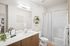 Pet-Friendly Apartments in West Phoenix, AZ - Acero Roosevelt - A Modern Bathroom with a Vanity, Sink, Large Mirror, Bathtub, Shower Curtain, Wall Shelving, and Soft Lighting.