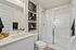 Two-Bedroom Apartments in Vancouver, WA - Bennington on First - A Bathroom with a Vanity, Sink, Mirror, Toilet, Glass-Enclosed Shower, Wall Art, and Towel Accents.
