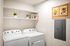 Pet-Friendly, Luxury Apartments in Eastmark, AZ - Acero Hawes Crossing - In-Home Laundry Room With Washer And Dryer, White Wall Shelving, Storage Decor, And Bright Overhead Lighting.