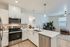 Three-BR Apartments in West Phoenix, AZ - Meritum Sheely Farms - Kitchen with Vinyl Plank Flooring, Quartz Counters, Stainless Steel Appliances, White Cabinets, a Kitchen Island, Modern Light Fixtures, a Ceiling Fan, the Living Room, and Stylish Decor