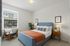 1 BR Apartments in Vancouver WA - Acero Jensen Park - Carpeted Bedrooom with a Bed, Wooden Armchair with Cushions, Wooden Nightstands with Drawers and Lamps, White Walls, and a Large Window