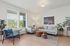 Vancouver, WA Pet-Friendly Apartments - Acero Jensen Park - Furnished Living Room with Grey Sofa, Armchair, and Wooden-Framed Armchair with Blue Cushions, Plants, Window, Wood-Style Flooring, and Wooden Coffee Tables