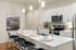 Three-BR Apartments in West Phoenix, AZ - Meritum Sheely Farms - Kitchen with Vinyl Plank Flooring, Quartz Counters, Stainless Steel Appliances, White Cabinets, a Kitchen Island, Modern Light Fixtures, a Ceiling Fan, the Living Room, and Stylish Decor