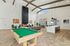 Luxurious open-plan living area with high ceilings, featuring a sleek pool table, modern fireplace, elegant lounge seating, and a contemporary kitchen island.