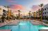 Apartments in Glendale, AZ, for Rent - Acero at the Stadium - Resort-Style Swimming Pool With Lounge Chairs, Palm Trees, and Community Buildings Surrounding The Water Under Colorful Sunset Sky.