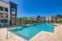 Luxurious apartment complex with a sparkling pool, shaded cabanas, and modern architecture under a clear blue sky.