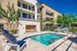 Luxurious apartment complex featuring a sparkling pool, elegant outdoor seating, and beautiful landscaping under a clear blue sky.
