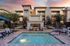 East Mesa, AZ, Apartments Near Dignity Health - Acero Eastmark - Pool Area With Spa, Outdoor Fireplace, Lounge Seating, Metal Fence, and Apartment Buildings.