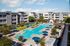 Inviting apartment complex with modern architecture features a luxurious swimming pool surrounded by sun loungers and vibrant blue umbrellas, perfect for a relaxing lifestyle.