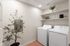 Modern laundry room with sleek washer and dryer, stylish floating shelves, and lush plant for a fresh, inviting atmosphere.