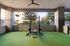 Modern outdoor gym area with state-of-the-art weightlifting equipment on vibrant green artificial turf, surrounded by elegant brickwork and lush greenery.