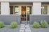 Modern apartment entrance with sleek sliding doors, contemporary exterior, and vibrant greenery lining the pathway.