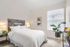 Vancouver, WA, Apartments with In-Unit Washer and Dryer - Acero Jensen Park - A Bedroom with Bedside Tables, Lamps, Wall Art, a Large Window, and Indoor Plants.