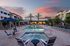 Luxurious apartment complex featuring a stunning pool surrounded by elegant lounge chairs and cabanas, set against a picturesque sunset sky.