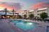 Luxurious apartment complex with a pristine swimming pool surrounded by elegant lounge chairs under a vibrant sunset sky.