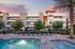 Elegant apartment complex with a sparkling pool, modern design, and palm trees under a vibrant evening sky.