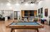 Modern open-concept living space featuring a sleek kitchen, stylish lounge area with multiple screens, and a classic billiards table for entertainment.